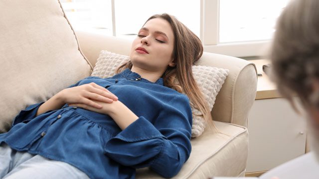 Young woman relaxing on couch during hypnosis therapy session for healing and self-discovery