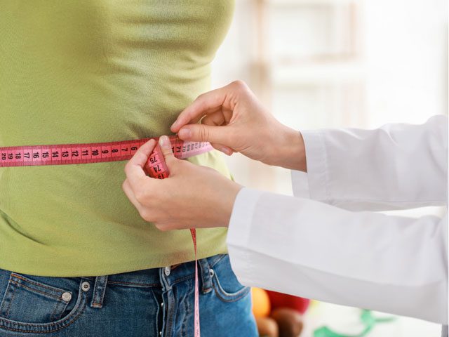 Close-up of waist measurement during a professional weight loss hypnosis session, tracking healthy progress and body transformation goals