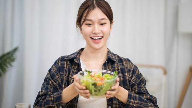 Smiling young woman holding a fresh salad bowl, enjoying healthy eating and positive lifestyle choices.